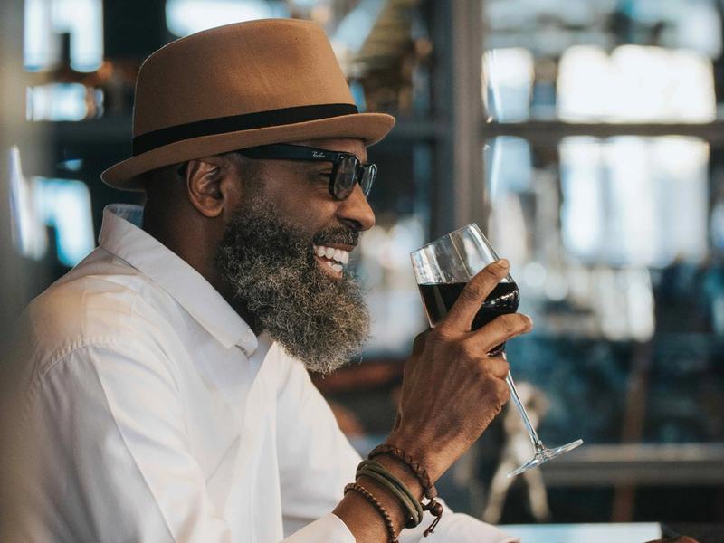 A man smiling while holding a glass of red wine at a restaurant bar.
