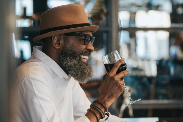 A man smiling while holding a glass of red wine at a restaurant bar.