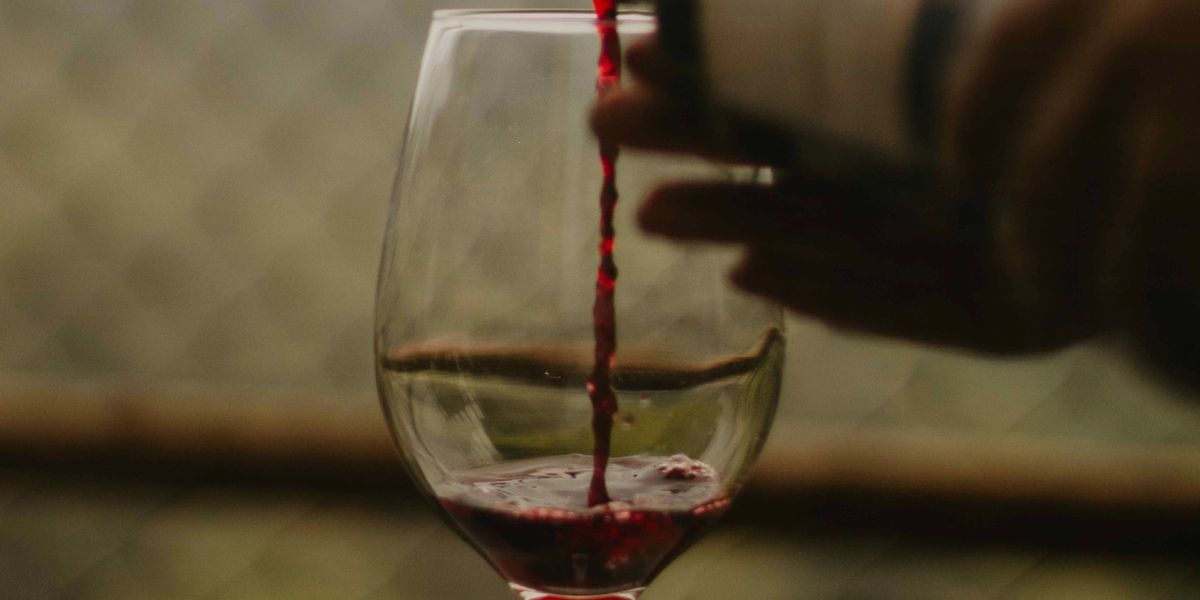 Red wine being poured into a glass, already partially filled.