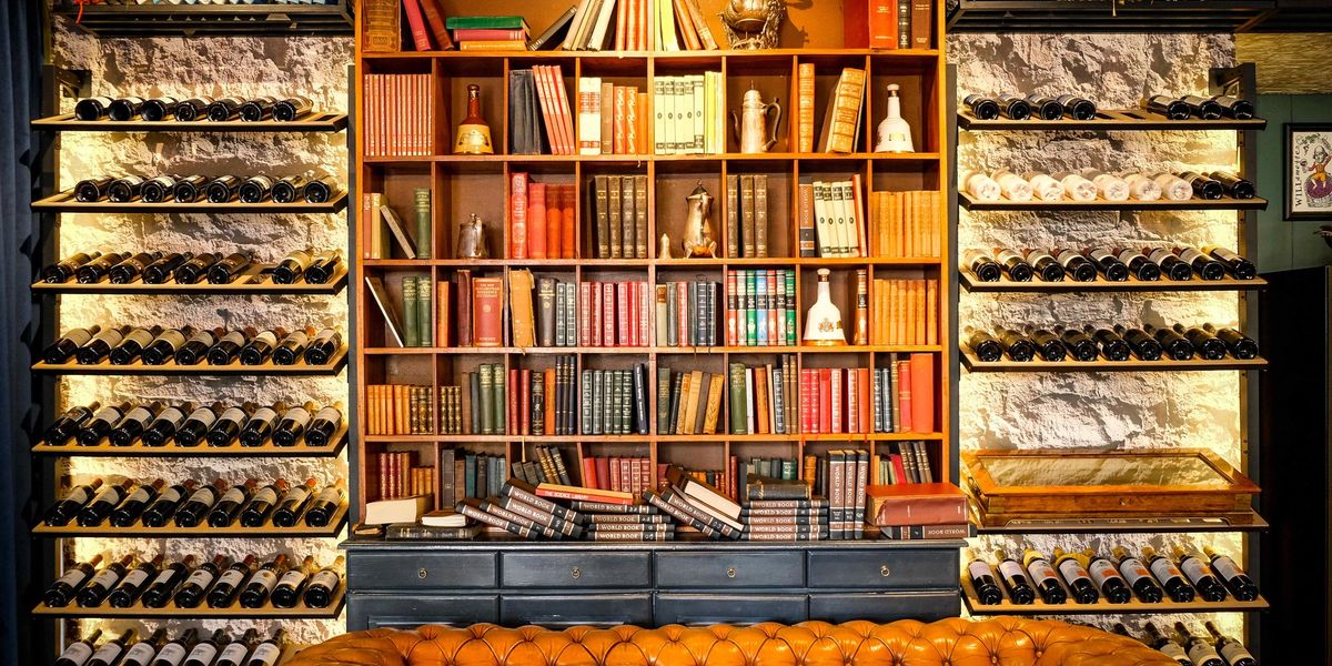 Open-shelf wine racks flanking a bookcase filled with books, decanters, and a leather sofa in a home library.
