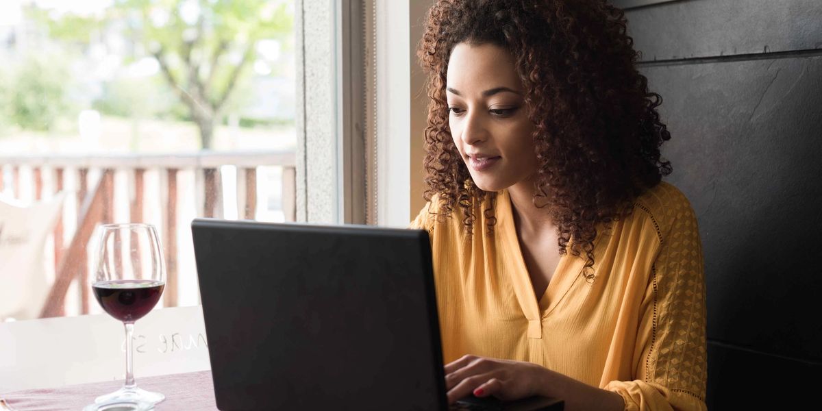 A woman using a wine collection app on her laptop with a glass of red wine beside her.