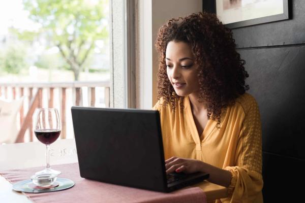 A woman using a wine collection app on her laptop with a glass of red wine beside her.