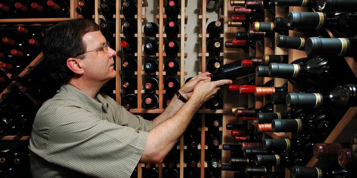 A man standing in a large wine cellar, searching for a specific bottle.