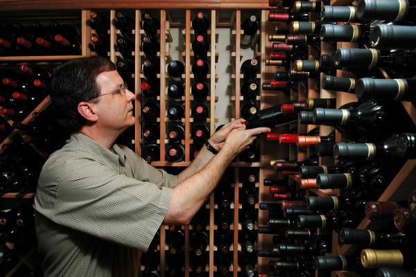 A man standing in a large wine cellar, searching for a specific bottle.