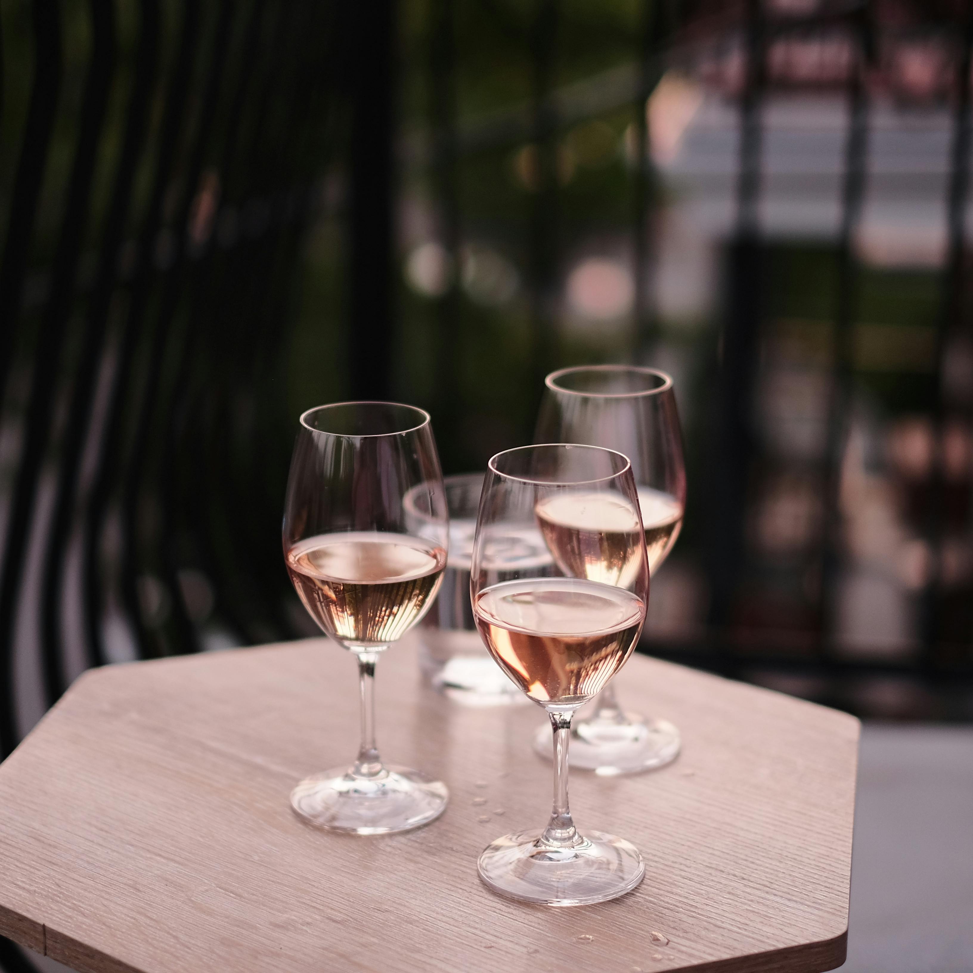 Three full glasses of rosé wine rest on a table on a terrace.