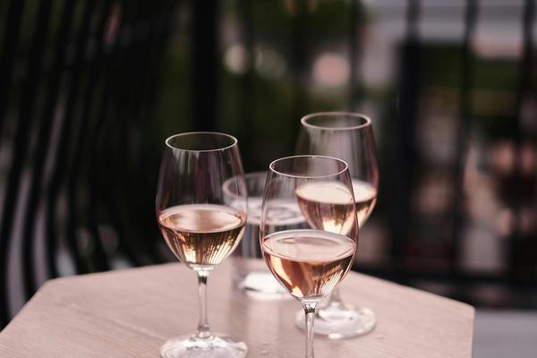 Three full glasses of rosé wine rest on a table on a terrace.