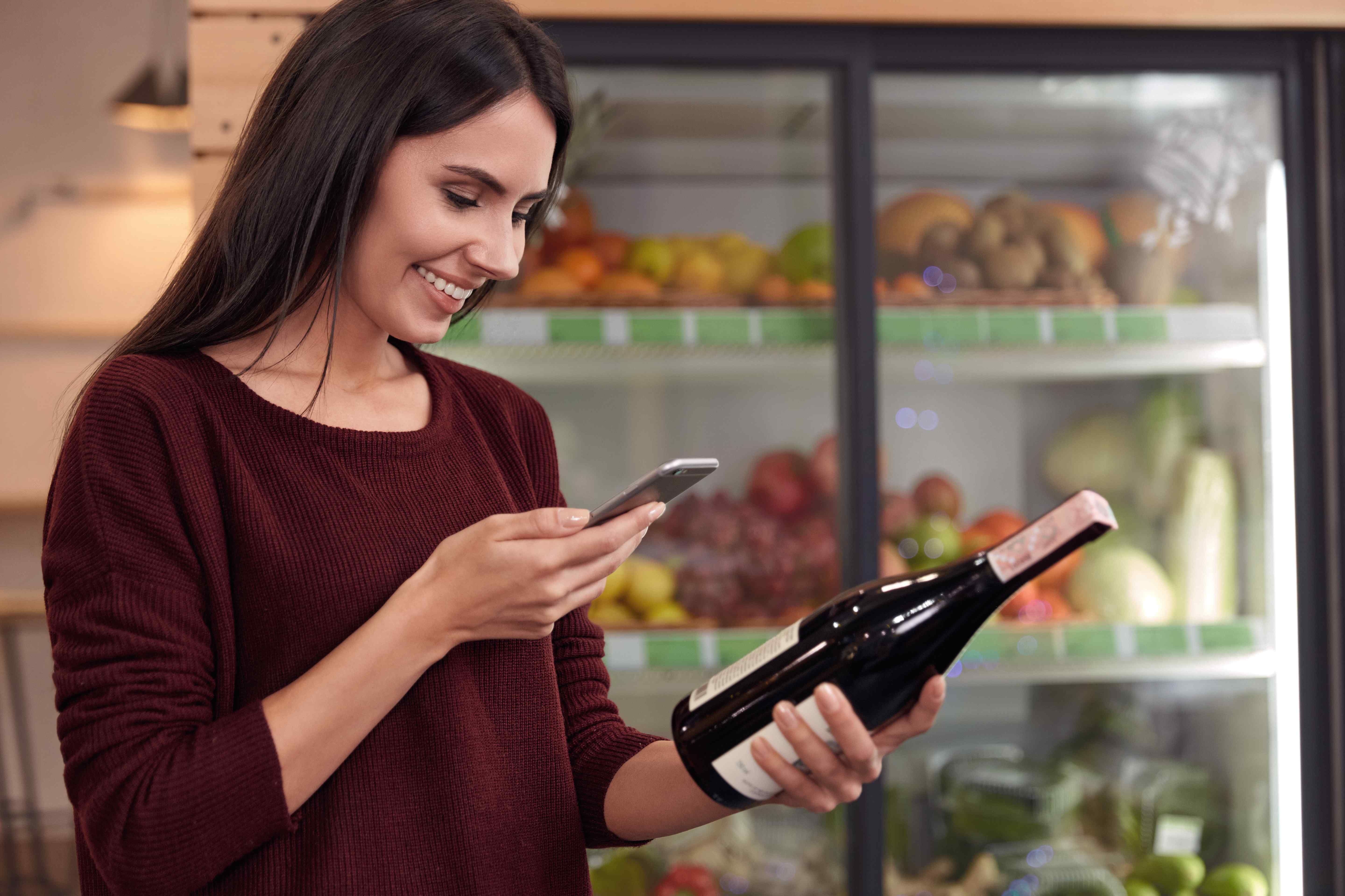 A woman scanning a wine bottle label with her iPhone in a grocery store.