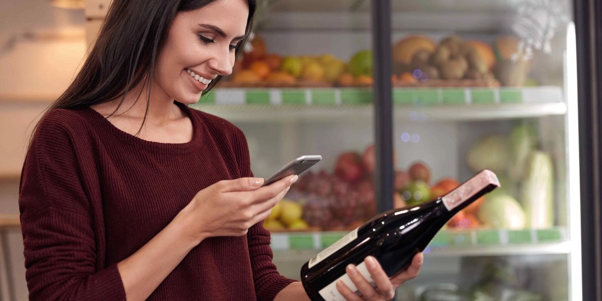A woman scanning a wine bottle label with her iPhone in a grocery store.