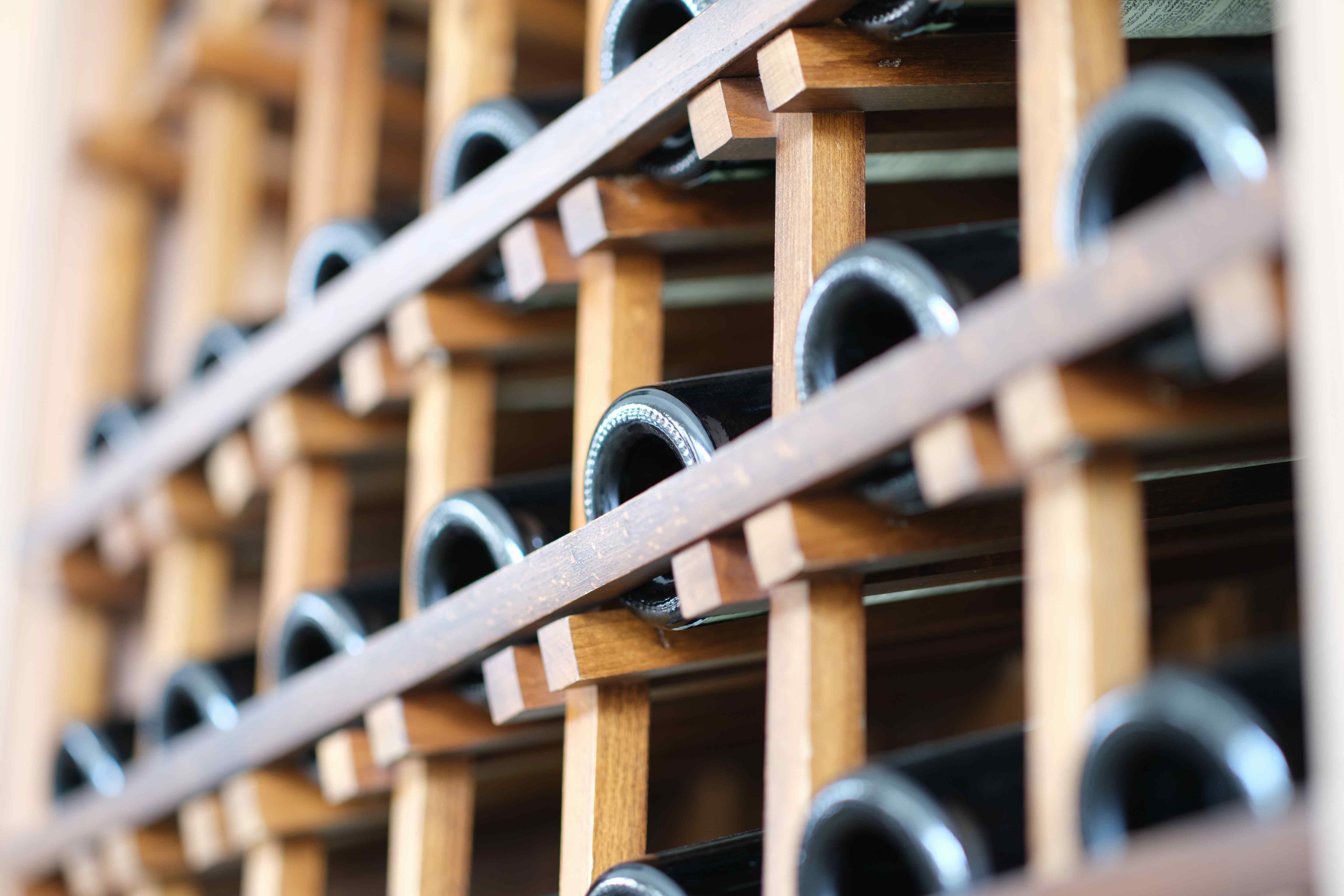 Dark glass wine bottles resting on their sides in a wooden lattice rack, viewed close up from the bottle bases.