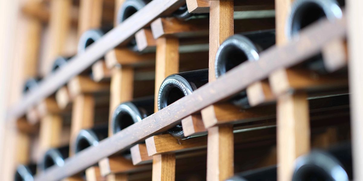 Dark glass wine bottles resting on their sides in a wooden lattice rack, viewed close up from the bottle bases.