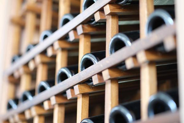 Dark glass wine bottles resting on their sides in a wooden lattice rack, viewed close up from the bottle bases.
