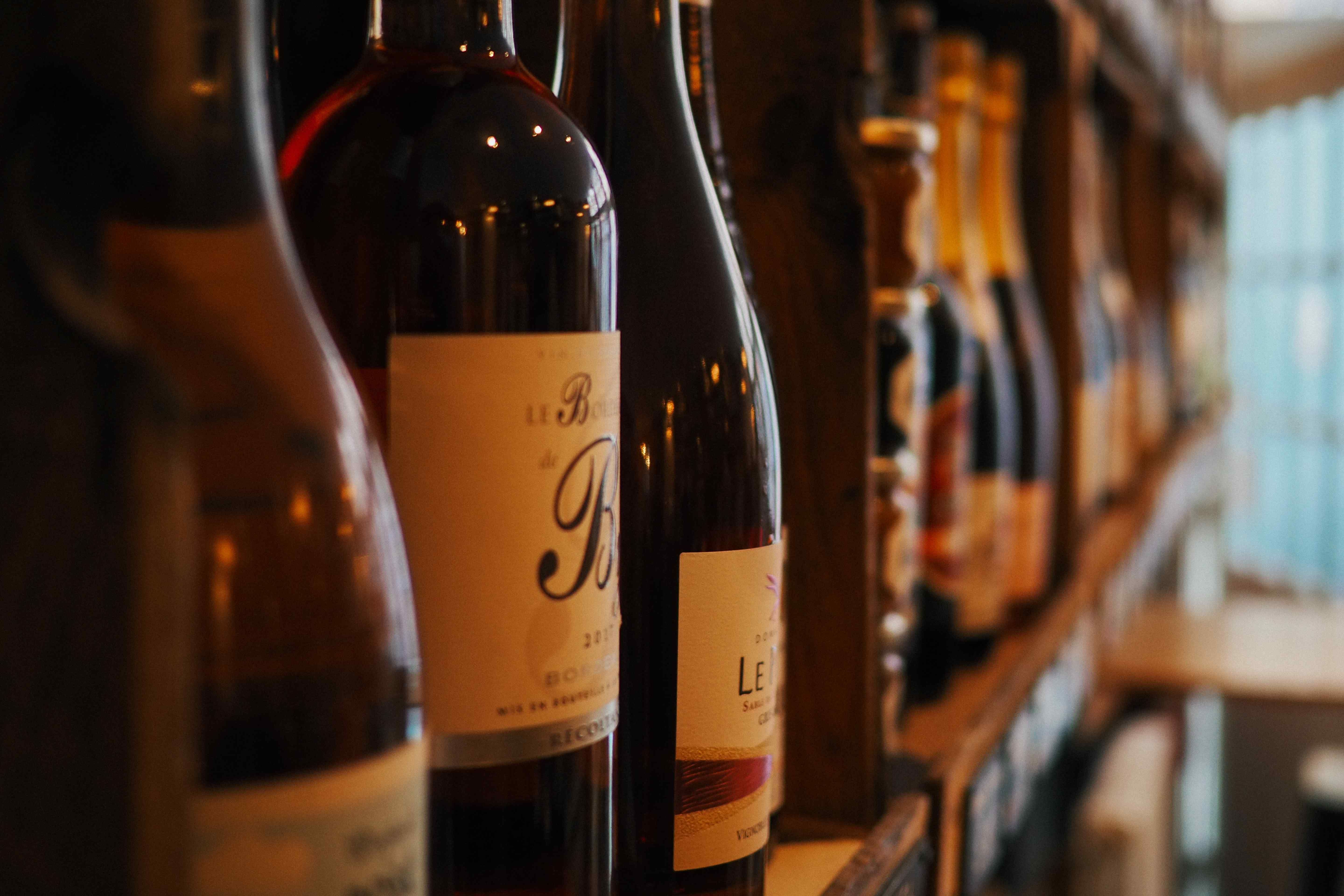 Close-up of wine bottles lined up on a wooden rack with labels facing forward.