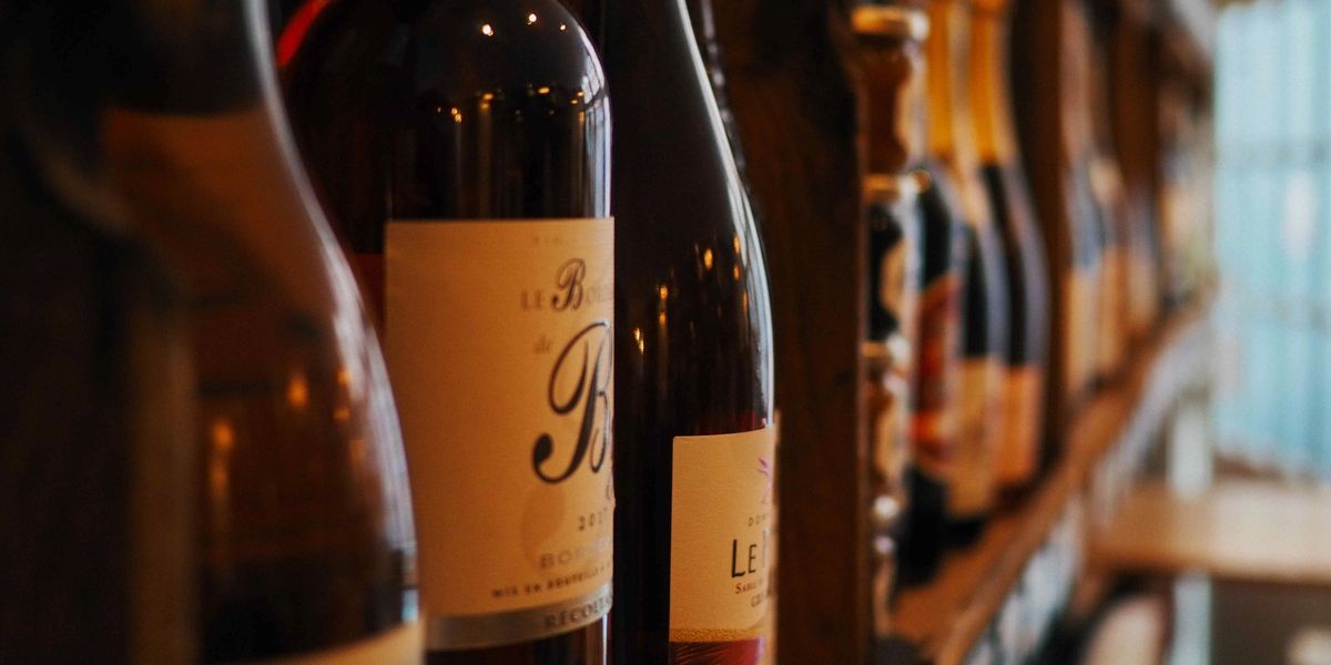 Close-up of wine bottles lined up on a wooden rack with labels facing forward.