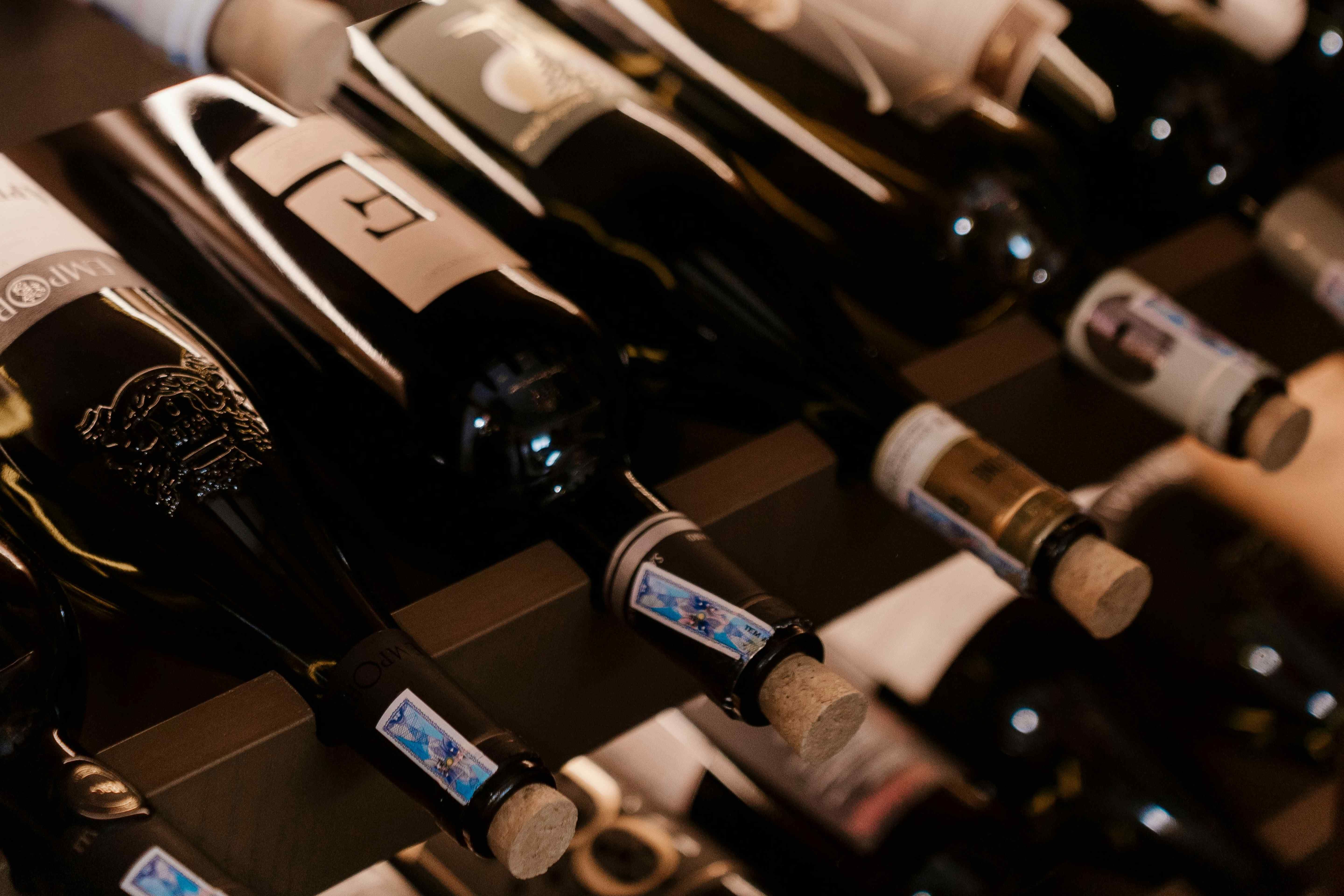 Wine bottles stored horizontally on cellar racks showing corks and labels up close.