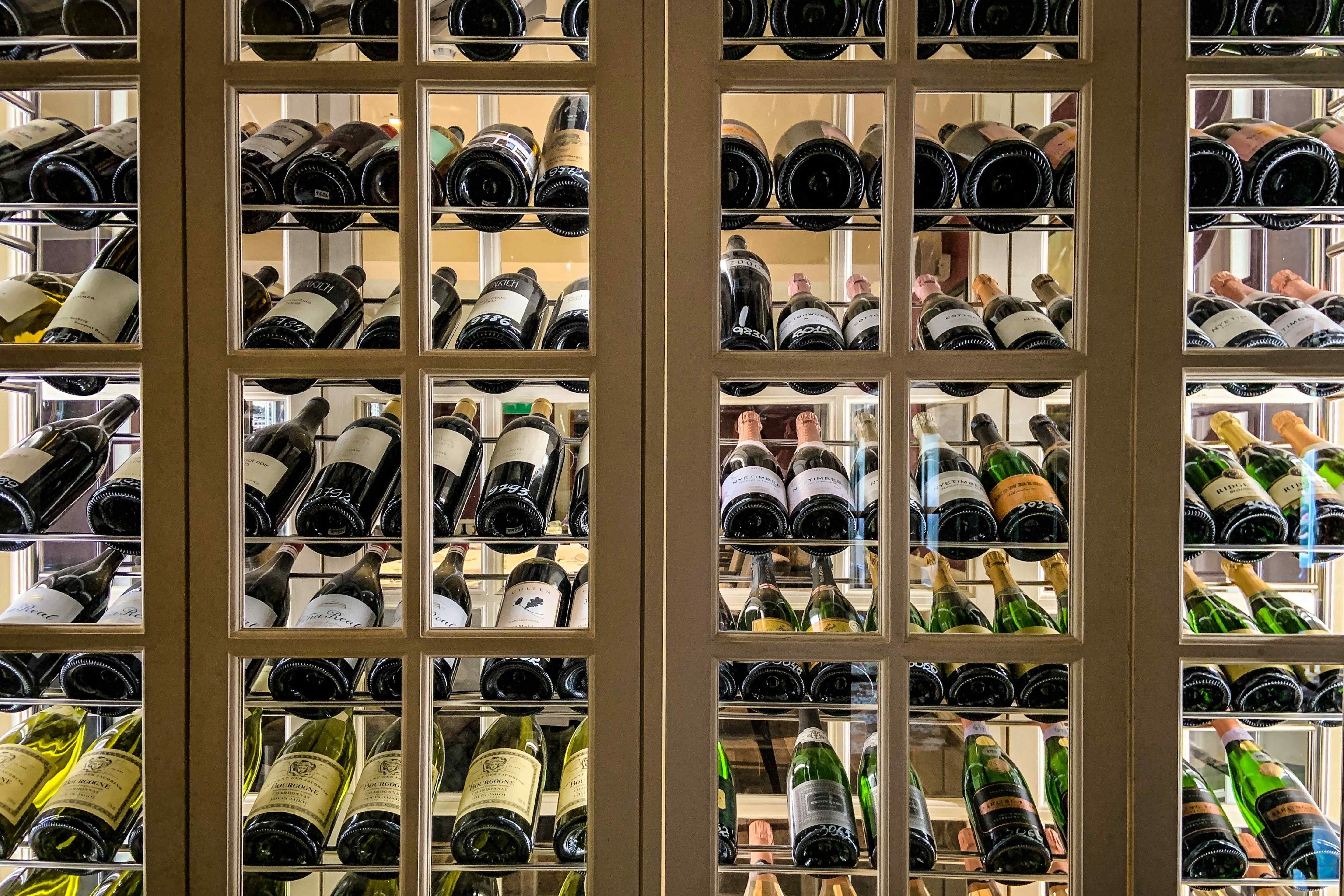 Glass-paned wine cellar cabinet displaying rows of labeled and numbered bottles including Champagne and Chardonnay.