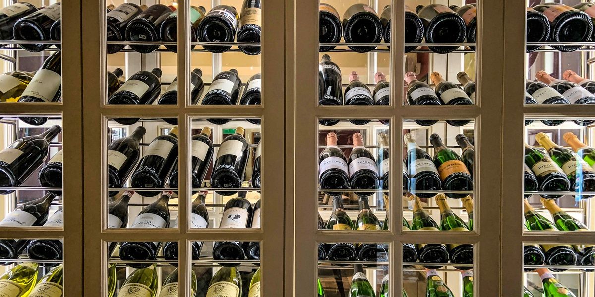 Glass-paned wine cellar cabinet displaying rows of labeled and numbered bottles including Champagne and Chardonnay.