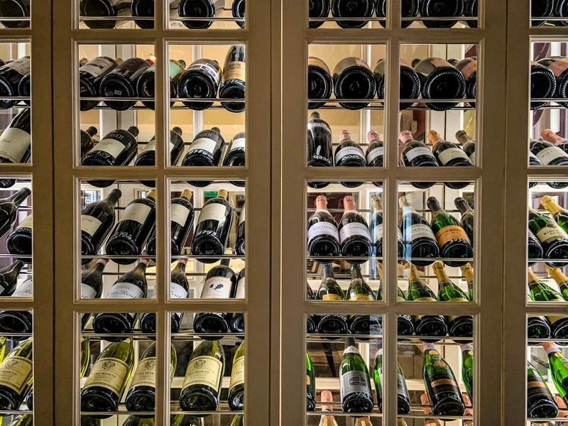 Glass-paned wine cellar cabinet displaying rows of labeled and numbered bottles including Champagne and Chardonnay.