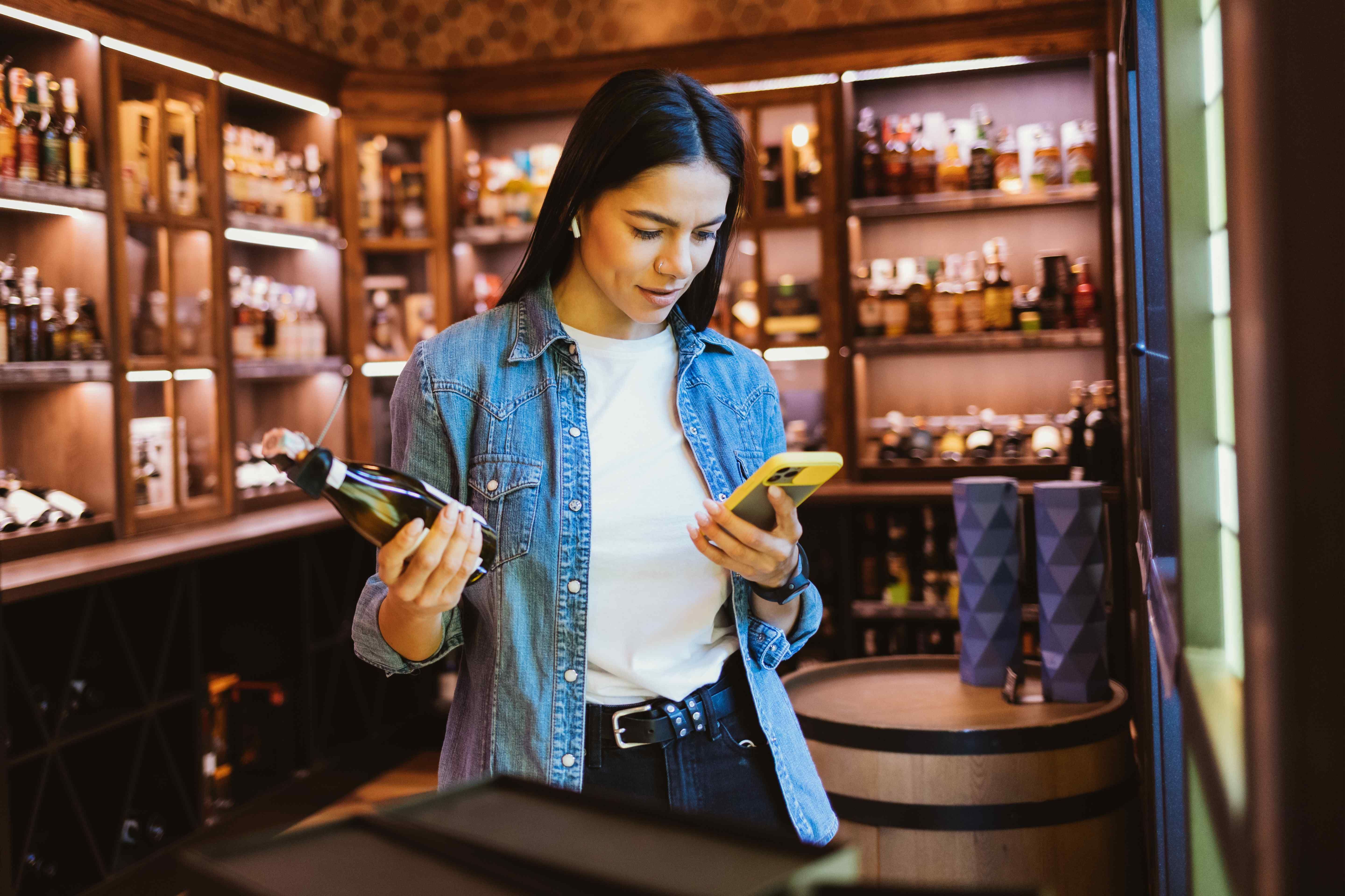 A woman scanning a wine bottle with her iPhone in a wine shop.