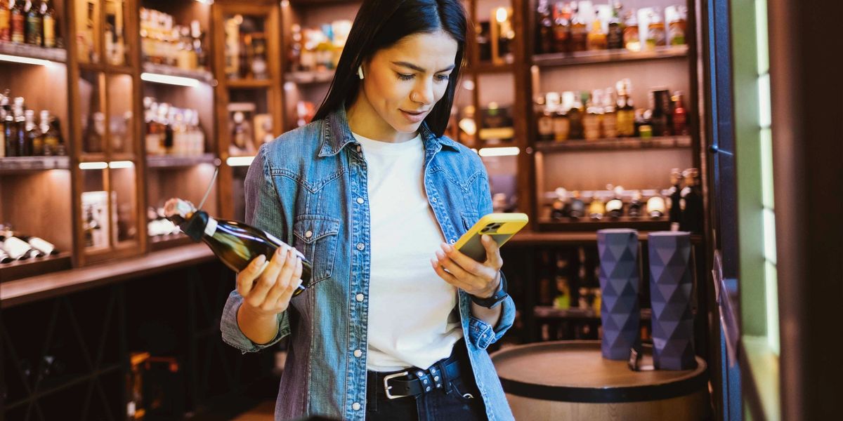 A woman scanning a wine bottle with her iPhone in a wine shop.