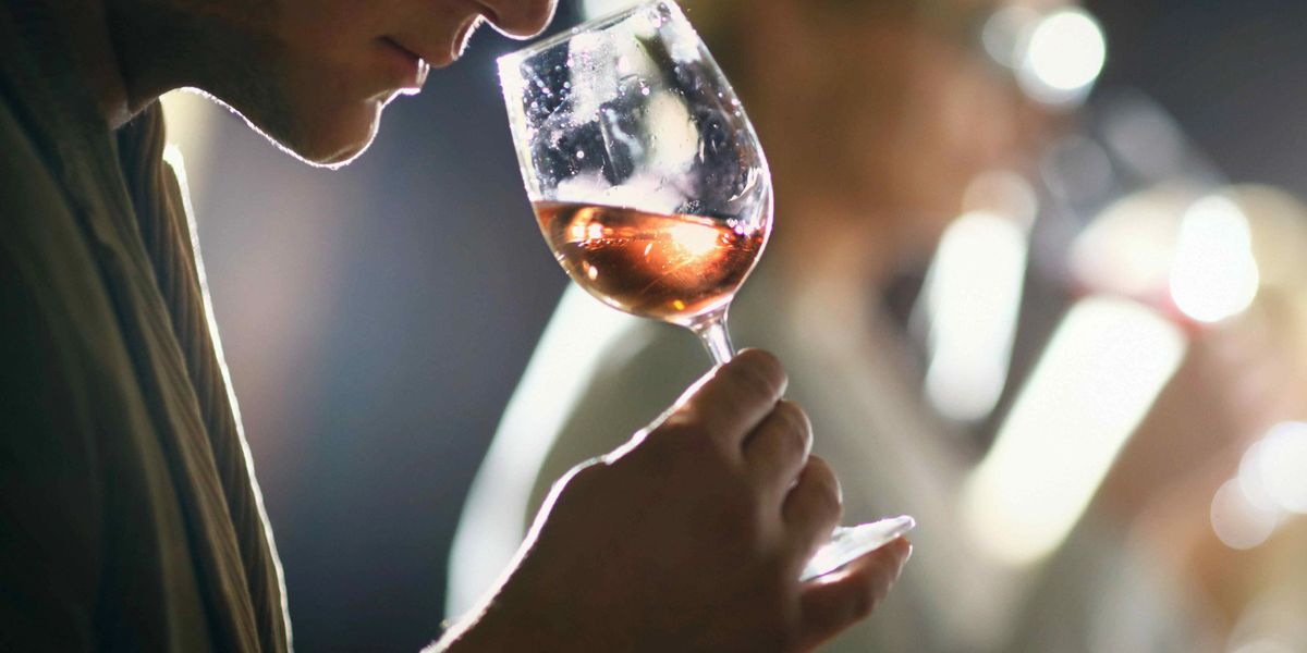 Person smelling a glass of rosé wine at a tasting, backlit with blurred figures in the background.