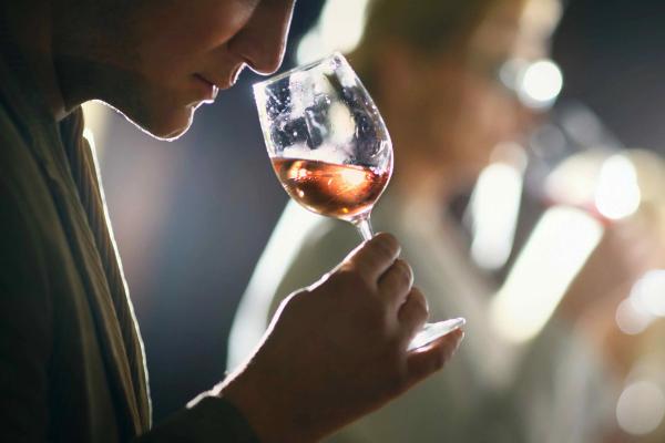 Person smelling a glass of rosé wine at a tasting, backlit with blurred figures in the background.