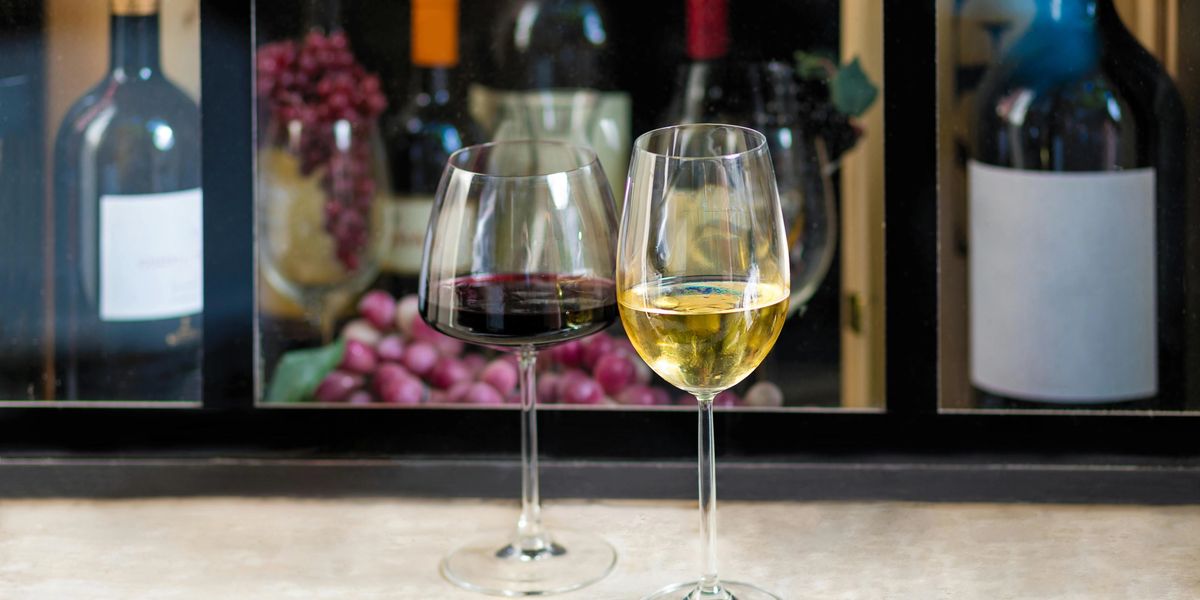 A full glass of red wine and a full glass of white wine rest on a table in front of a wine display shelf.