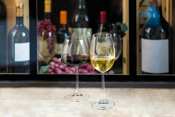A full glass of red wine and a full glass of white wine rest on a table in front of a wine display shelf.
