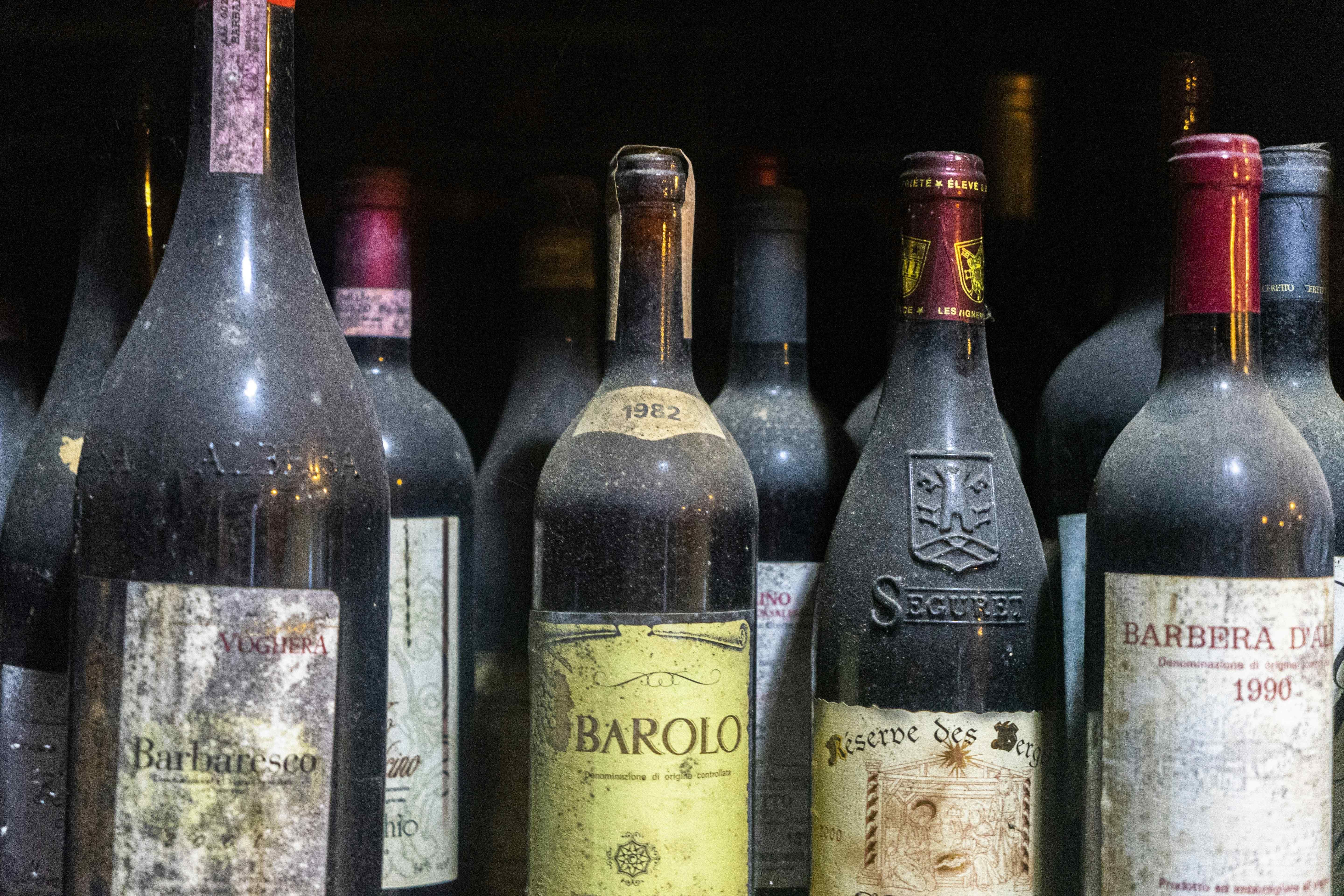 Dusty aged wine bottles including a 1982 Barolo and 1990 Barbera d'Alba with faded cellar labels.