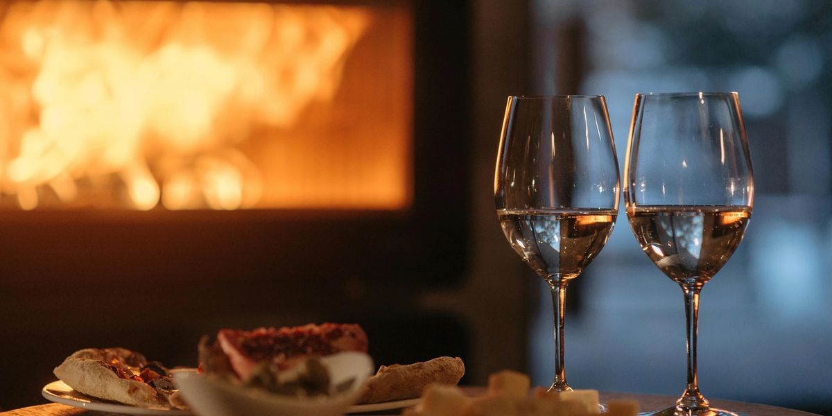 A cozy scene: snacks and full wine glasses sit on top of a coffee table in front of a roaring fireplace.