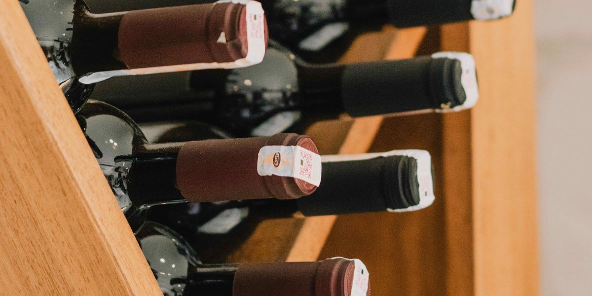 Red wine bottles fill a shelf in a wine cellar.