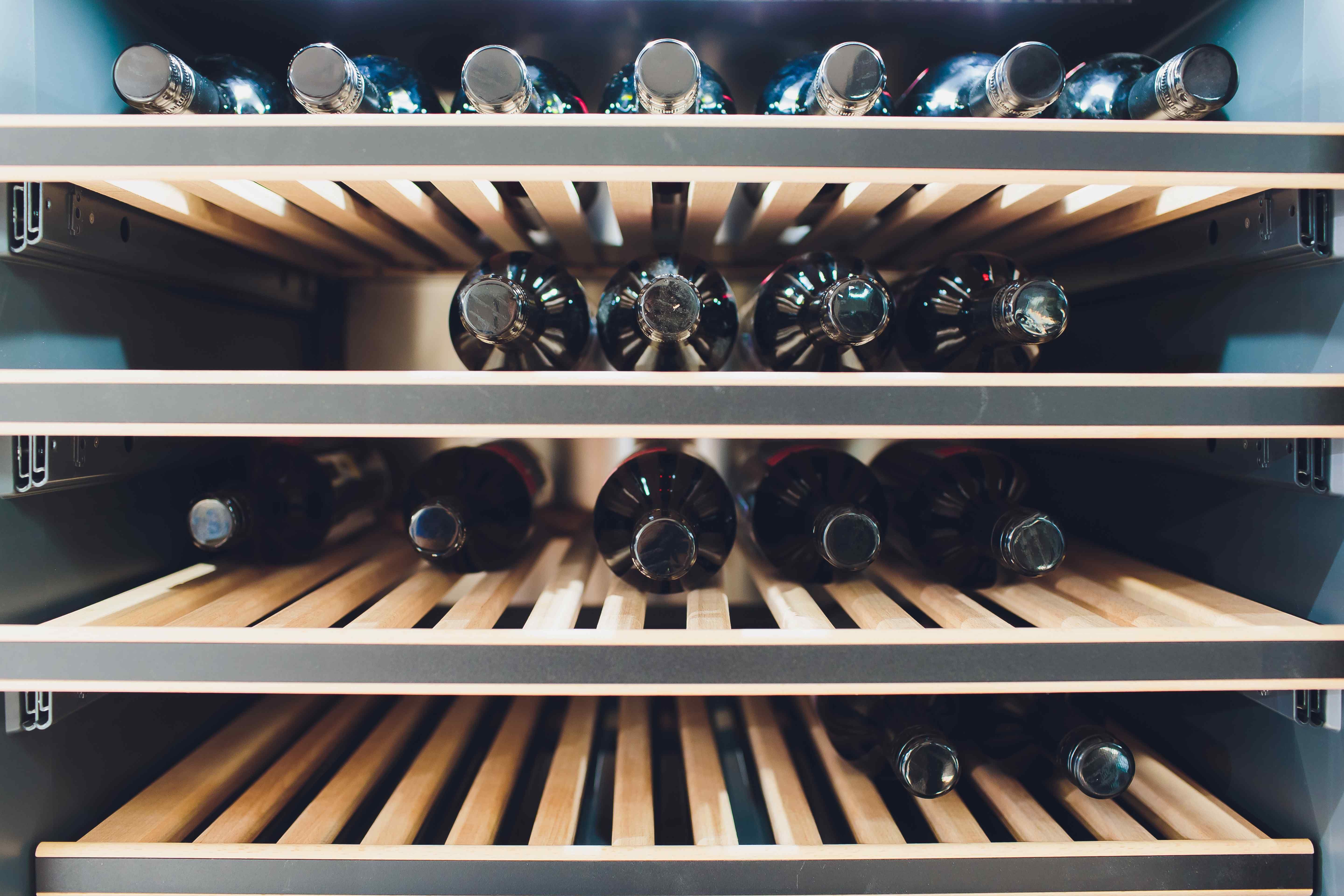 Wine bottles stored horizontally on wooden shelves inside a wine fridge.