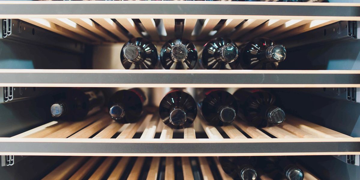 Wine bottles stored horizontally on wooden shelves inside a wine fridge.