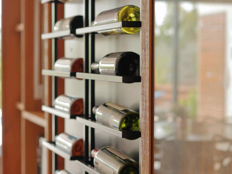 A modern wall-mounted metal wine rack displaying bottles horizontally in a contemporary space.