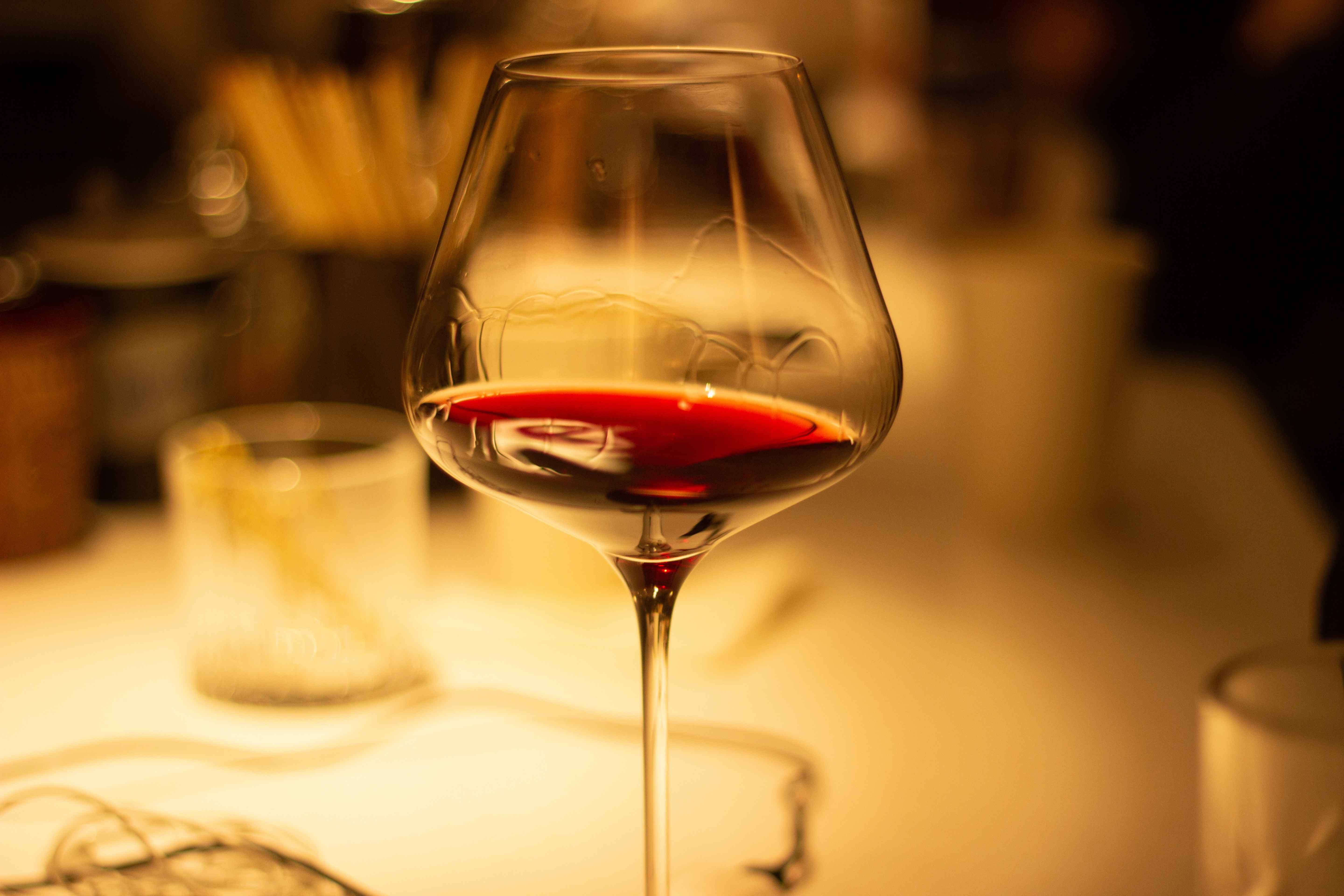 Glass of red wine on a table in warm low light, showing wine legs running down the inside of the bowl.