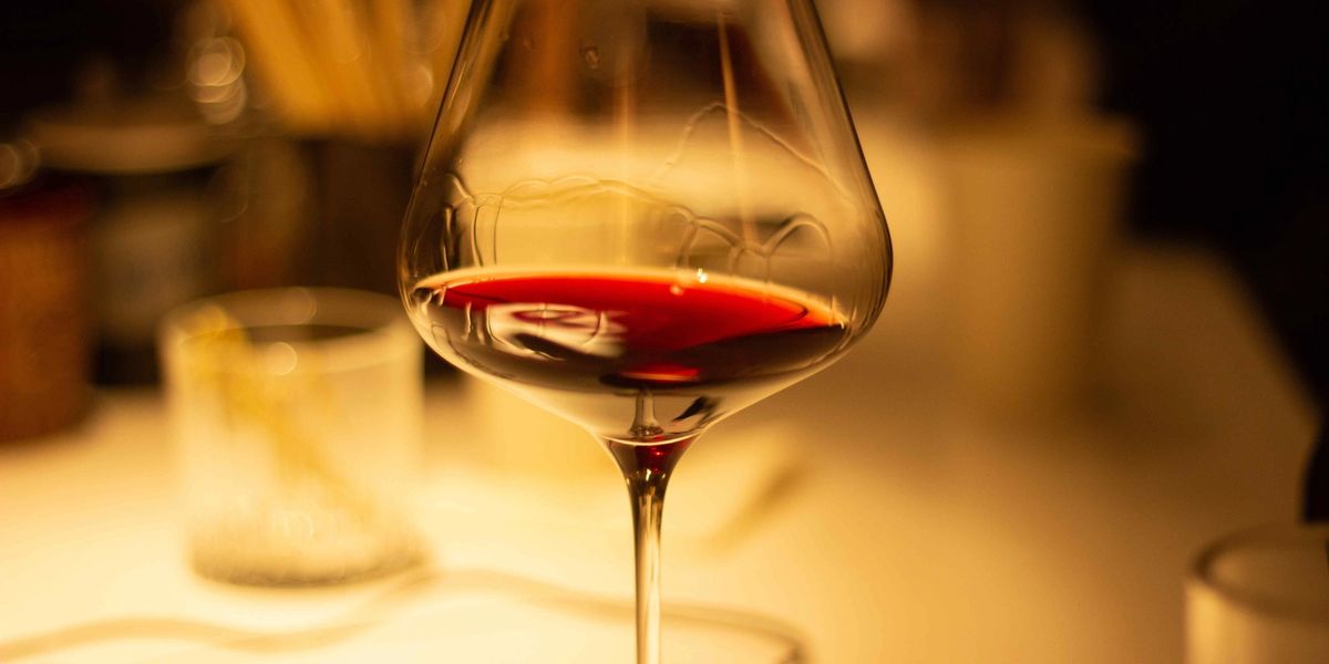 Glass of red wine on a table in warm low light, showing wine legs running down the inside of the bowl.