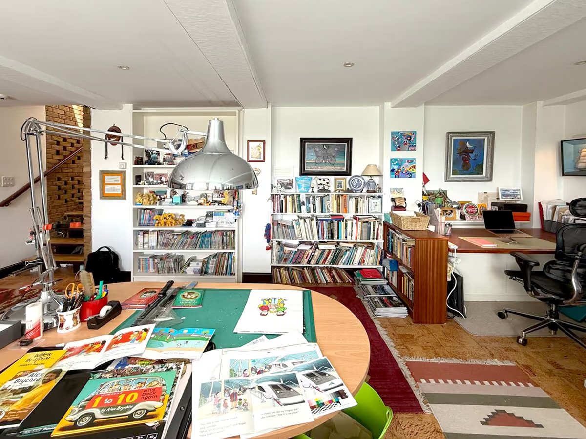 Alex Brychta's illustration studio with a drawing desk covered in sketches, bookshelves of his children's books, and framed artwork on the walls