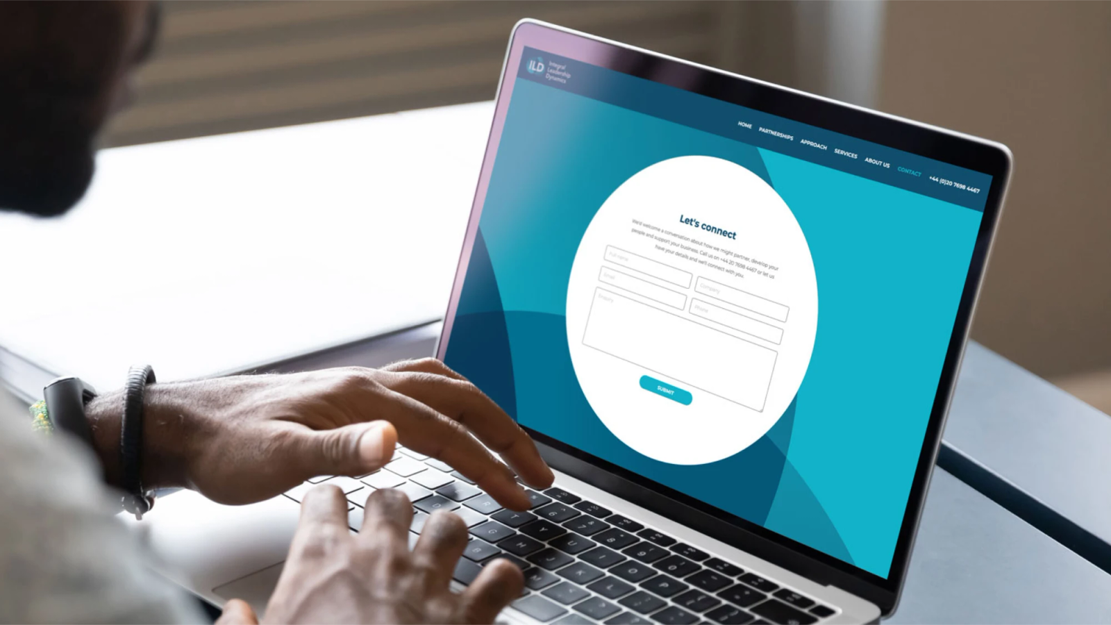 A person typing on a laptop displaying the Integral Leadership Dynamics website's 'Let's connect' contact form