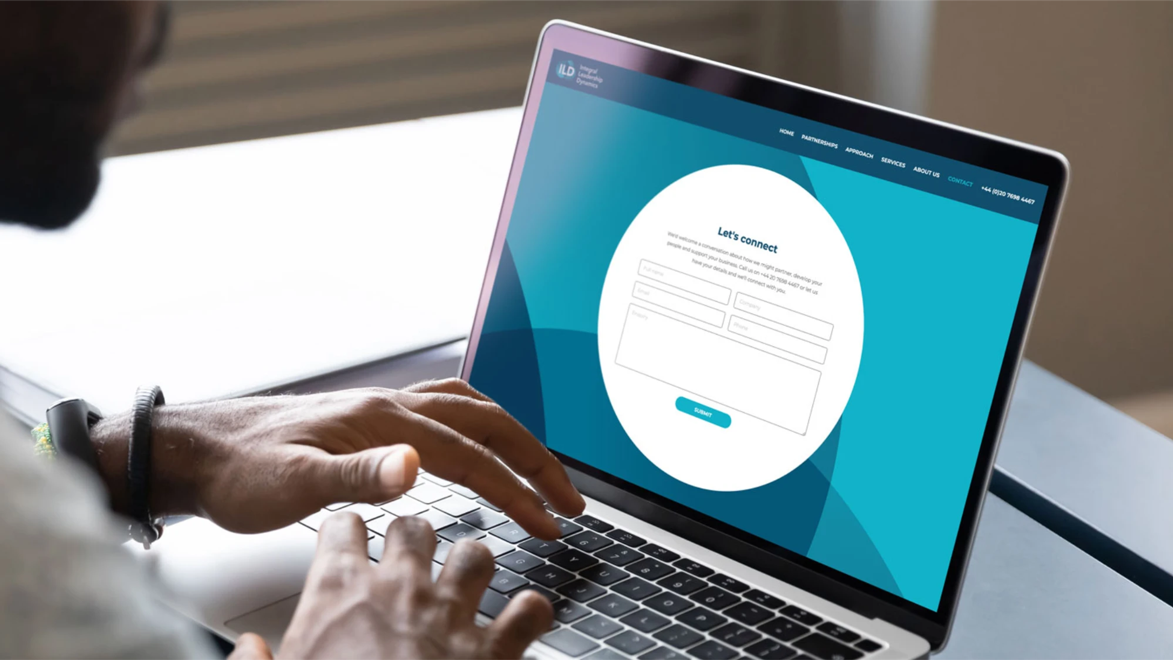 A person typing on a laptop displaying the Integral Leadership Dynamics website's 'Let's connect' contact form
