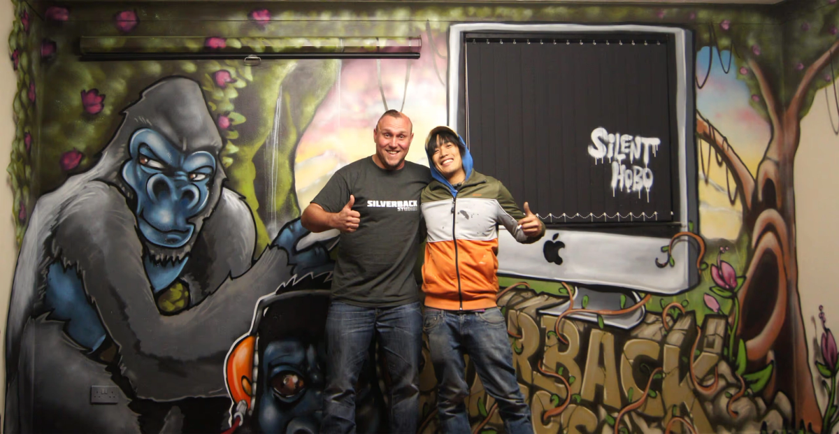 Mal and another man standing in front of some graffiti of a Gorilla
