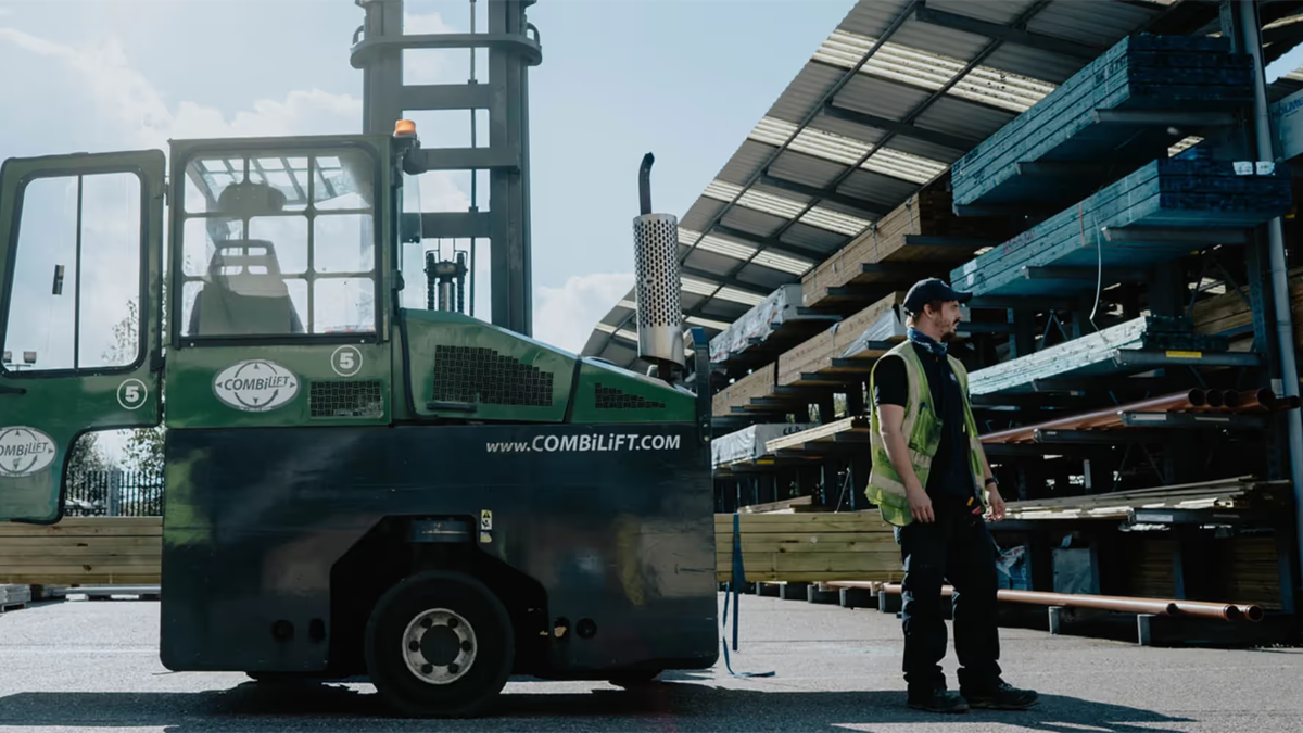 A Combilift sideloader forklift truck parked beside a yard worker among racked timber at a builders merchant