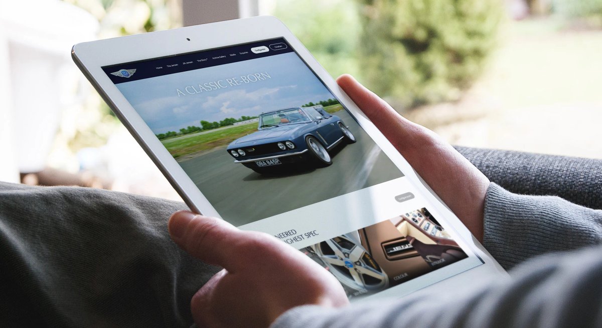 A person holding a tablet displaying the JIA Jensen website homepage with the headline 'A Classic Re-Born'