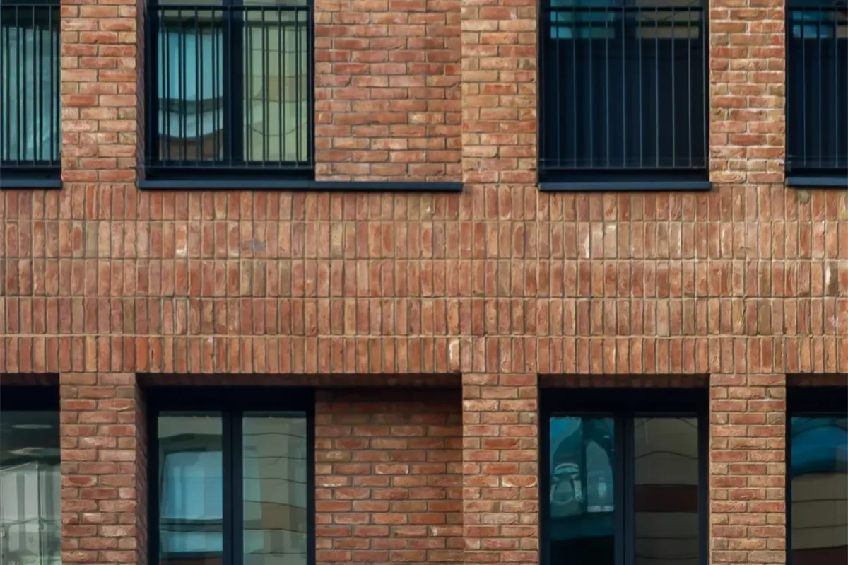 Close-up of a textured red brick building facade with black-framed windows