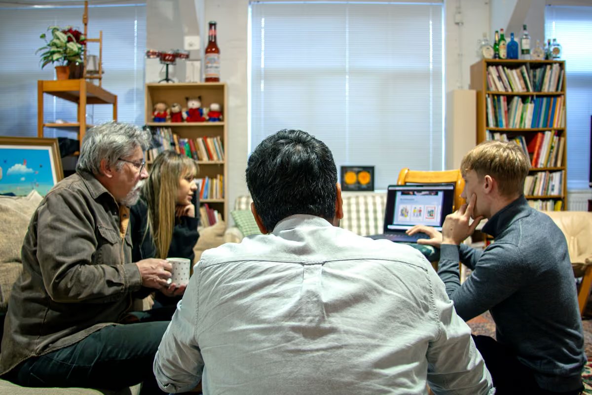 Alex Brychta and colleagues gathered around a laptop reviewing illustration artwork during a project meeting