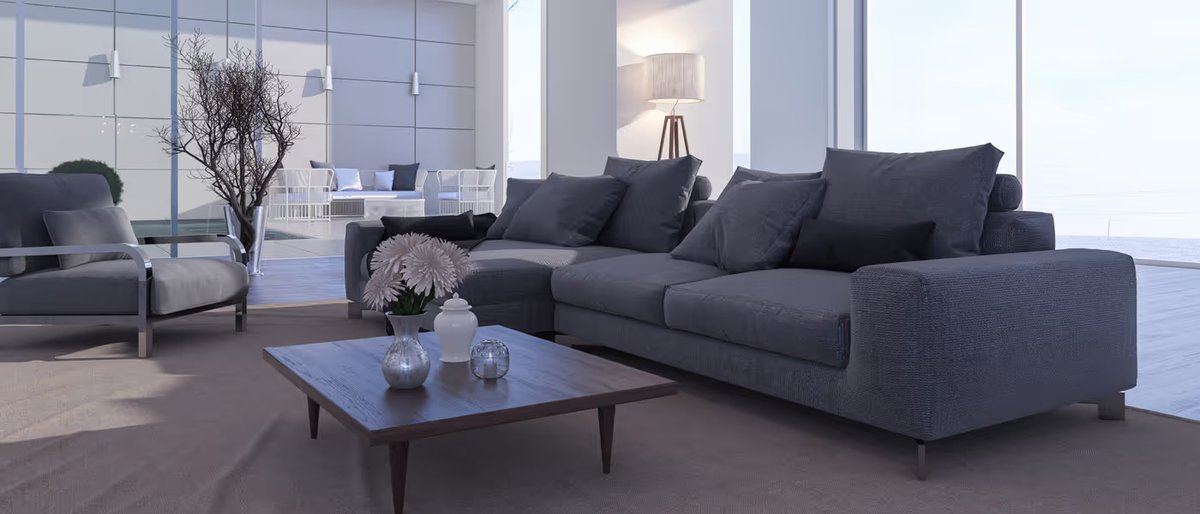 A grey corner sofa and armchair in a living room with floor-to-ceiling windows overlooking the sea