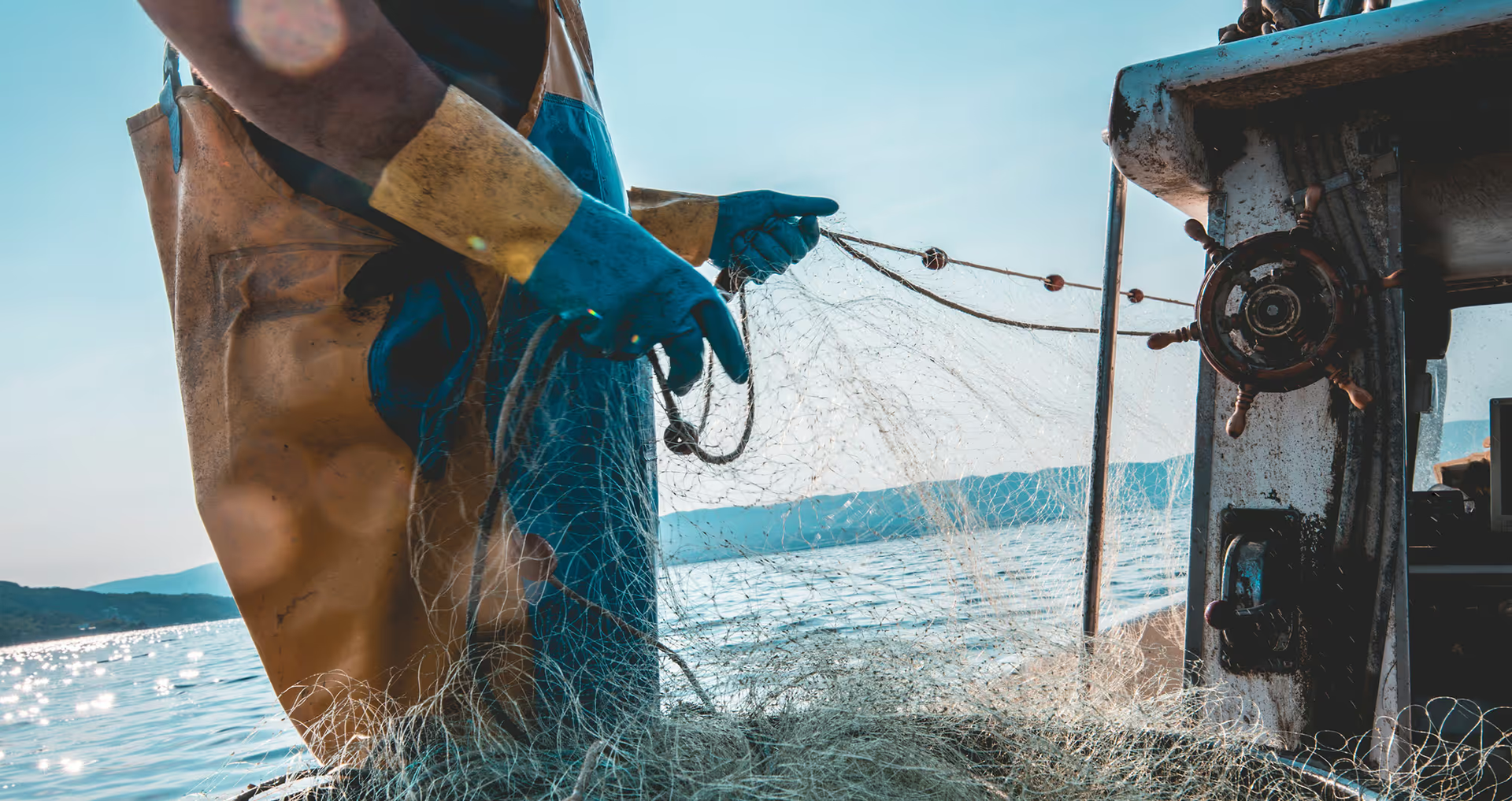 A close up shot of a man pulling in a net on a fishing trawler out at sea on a sunny day