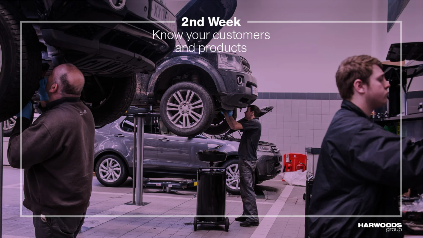 Two colleagues reviewing diagnostics on a laptop beside a car on a ramp, with '1st Day: Finding your way around' overlay text