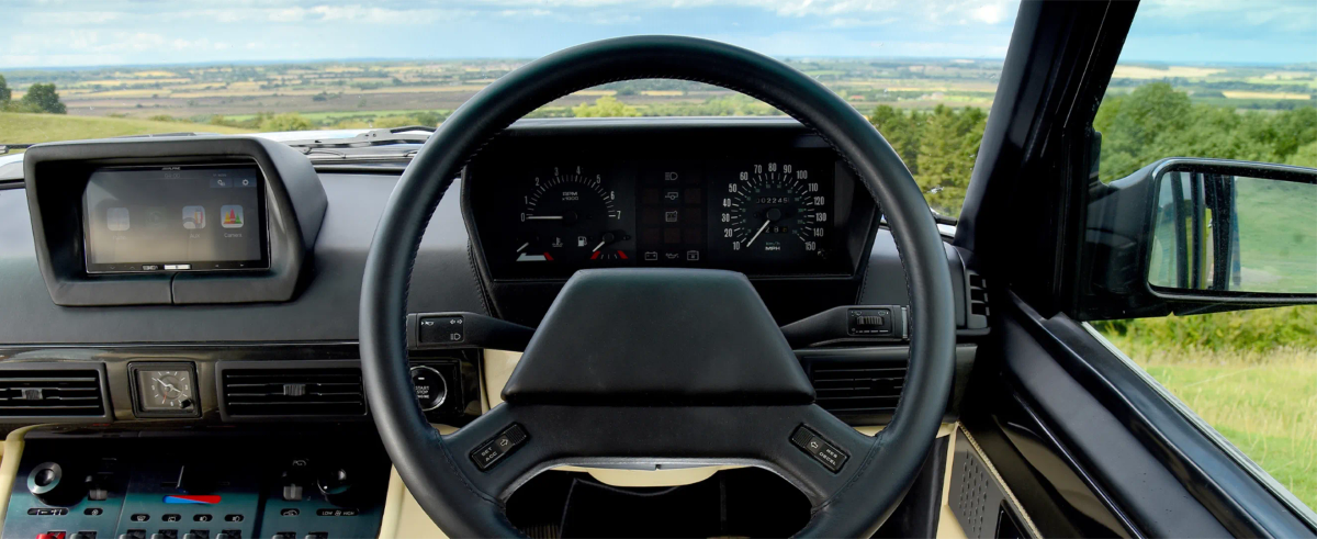 The leather steering wheel and dashboard of a Range Rover Chieftain, with rolling countryside visible through the windscreen
