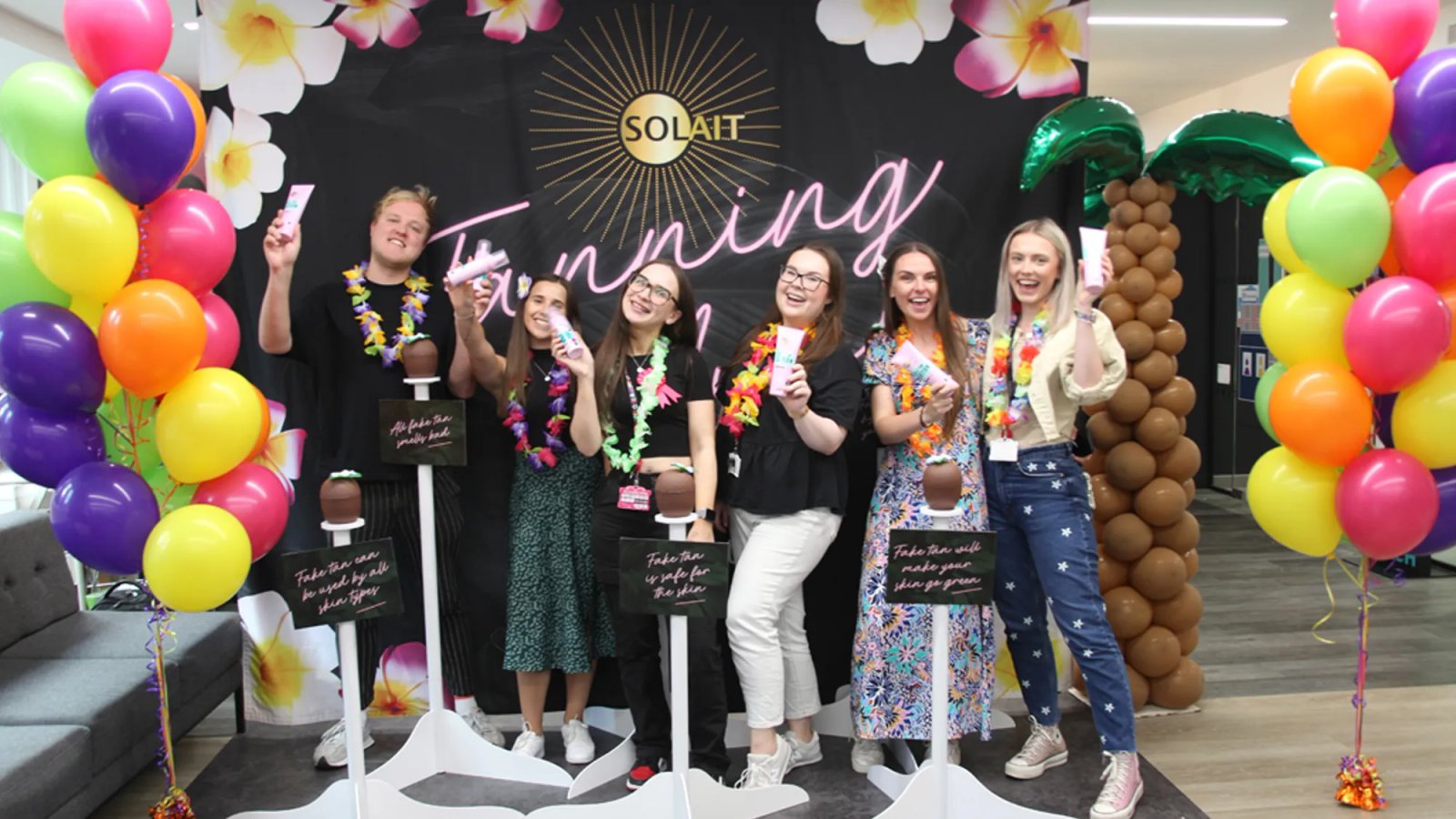 The Solait presentation team posing with their products on a tropical branded backdrop with balloons and inflatable tropical plants around.