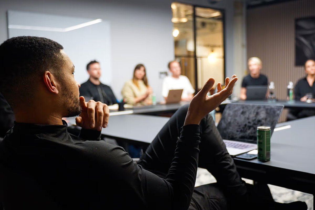 Steven Bartlett sat a table with team members, talking and gesticulating