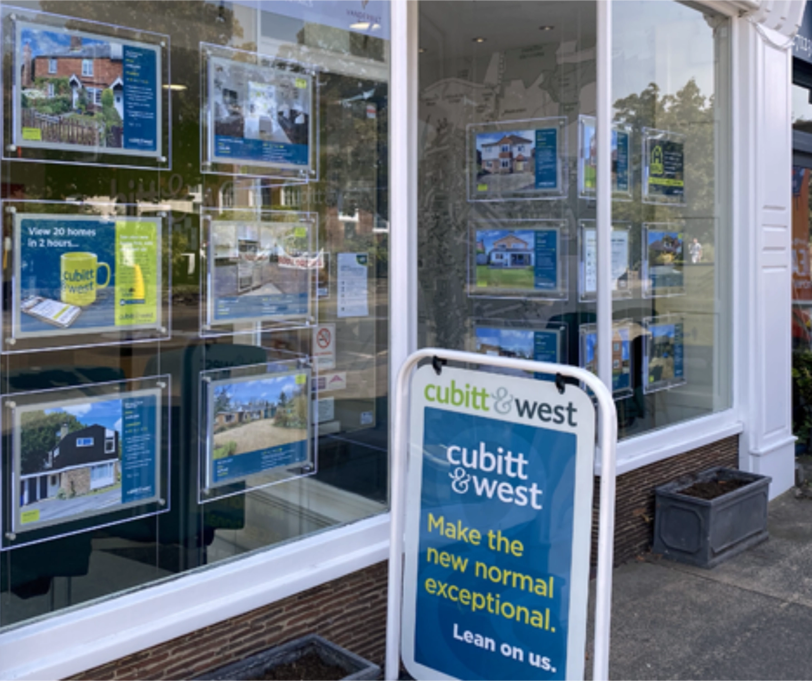 The exterior of a Cubitt & West estate agency branch, with property listings displayed in the window and a sandwich board reading 'Make the new normal exceptional, lean on us'